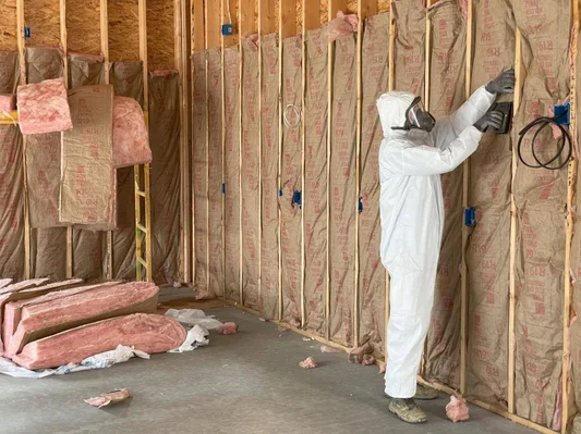 Installer fitting pink fiberglass batt insulation in wall studs